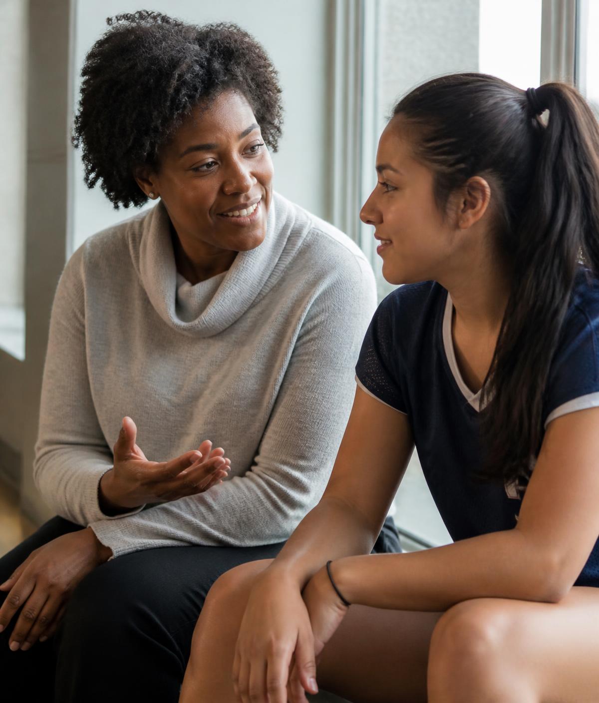 A mentor talking with a student-athlete on bleachers